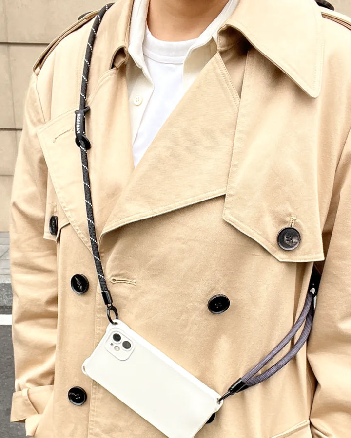 Close up of an adjustable nylon rope phone leash in black and white worn over a beige coat#color_black
