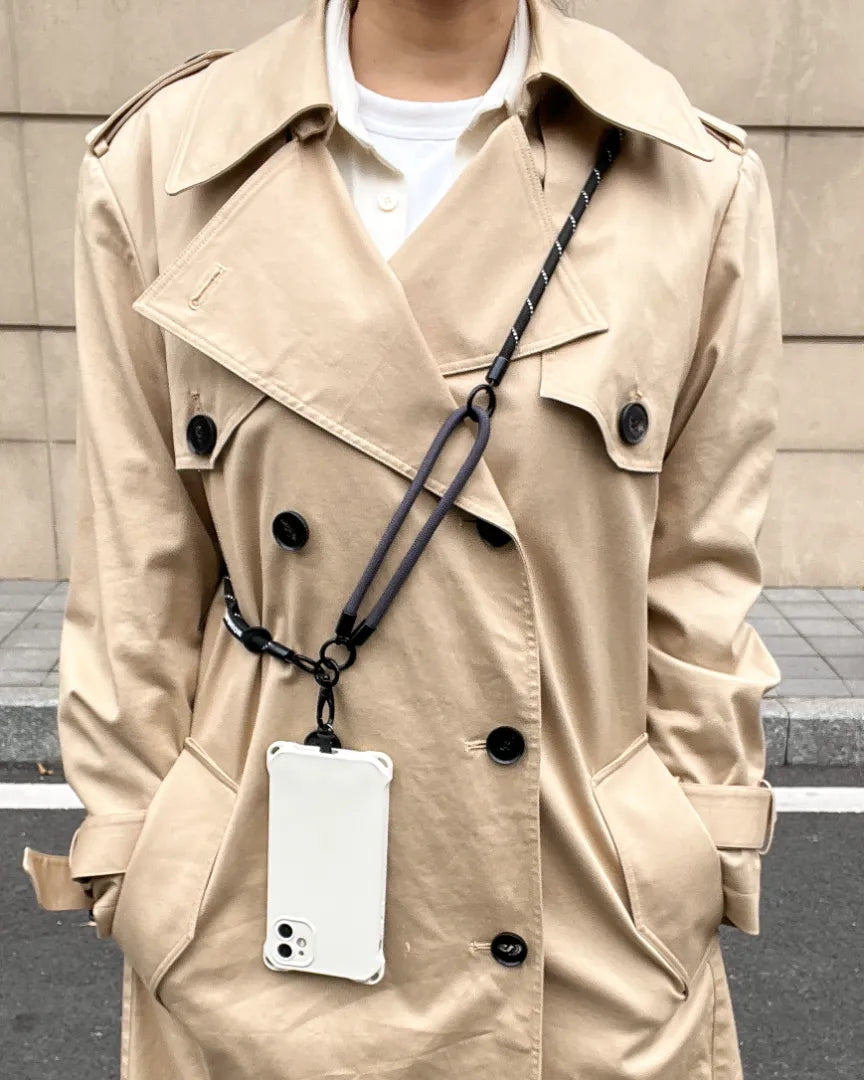Modern woman wearing a sleek black crossbody phone strap over a beige trench coatl#color_black