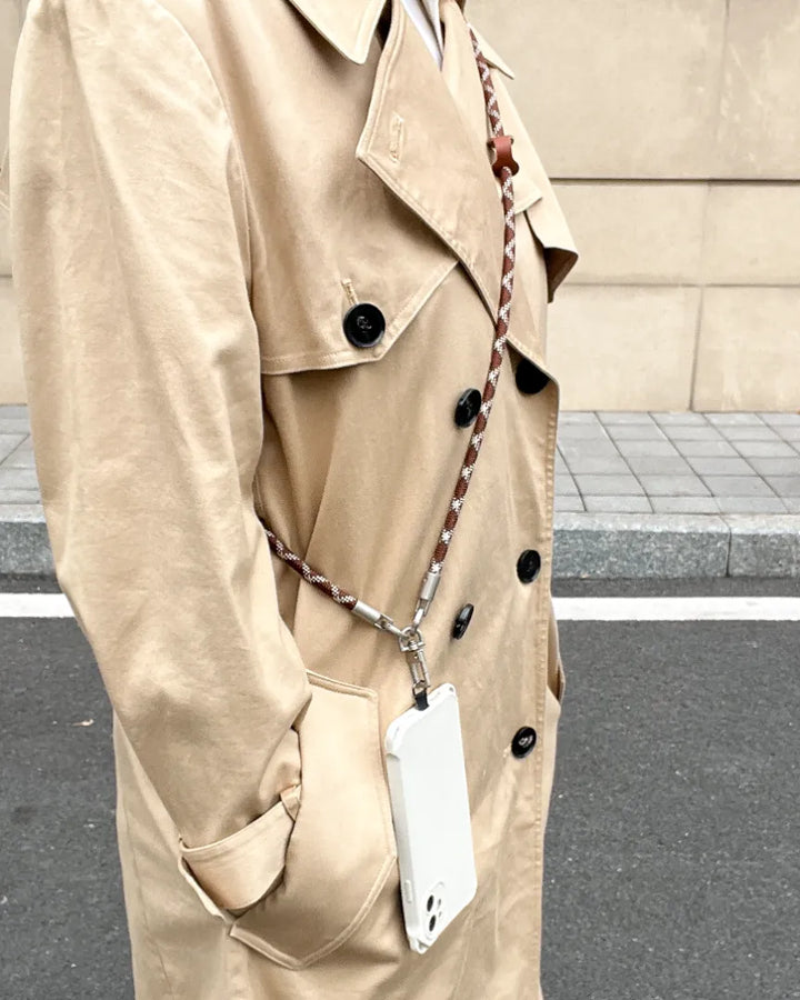 Model wearing a brown and white crossbody phone lanyard paired with a classic trench coat#color_brown