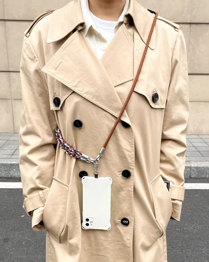 Fashionable woman wearing a brown leather crossbody phone strap over a classic trench coat#color_brown
