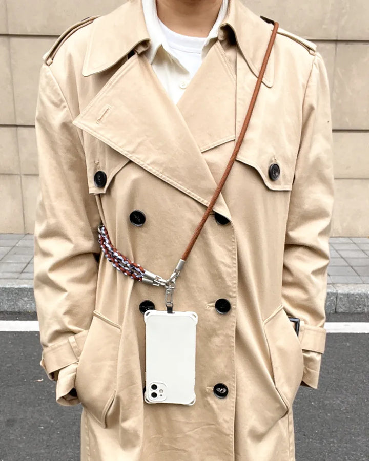 Fashionable woman wearing a brown leather crossbody phone strap over a classic trench coat#color_brown