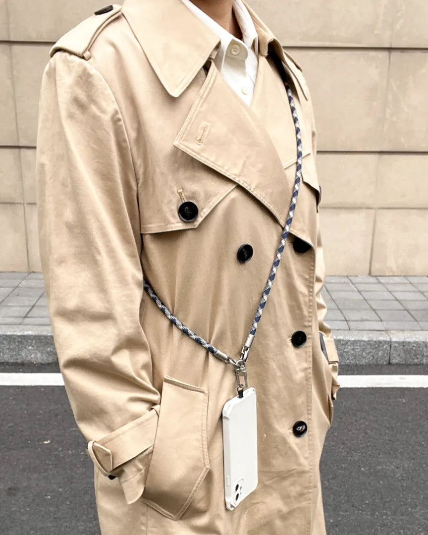 Model wearing a patterned crossbody phone strap paired with a classic trench coat#color_blue