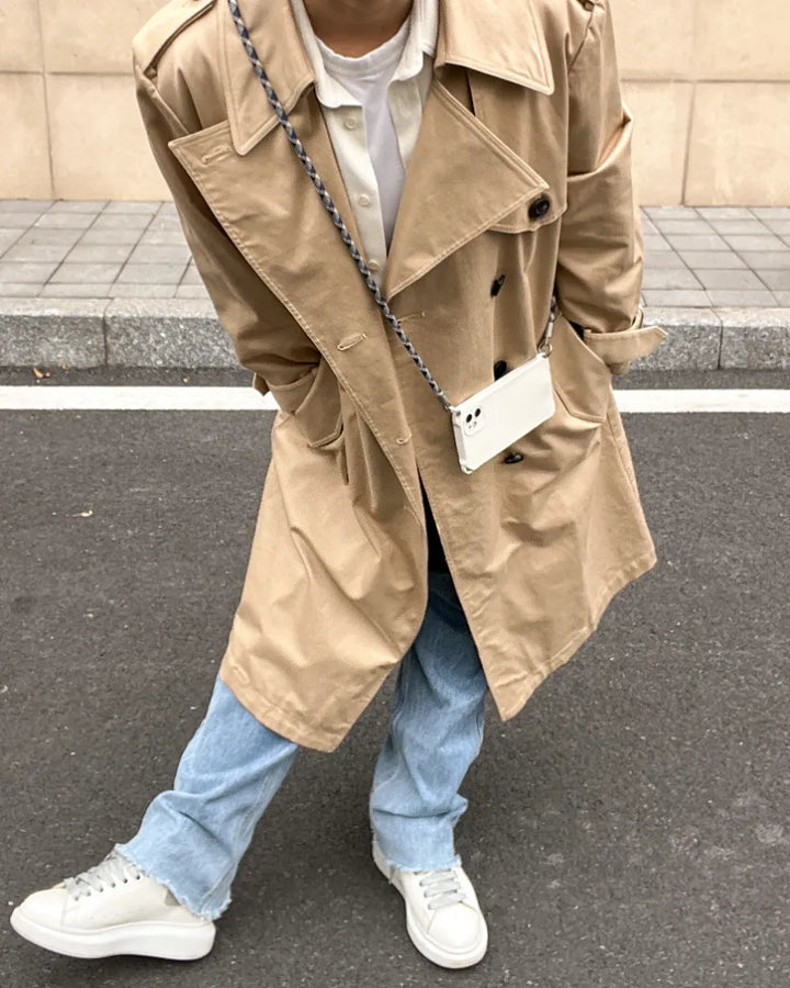 Outdoor lifestyle shot of a woman using a brown and white phone lanyard with a classic trench coat#color_blue