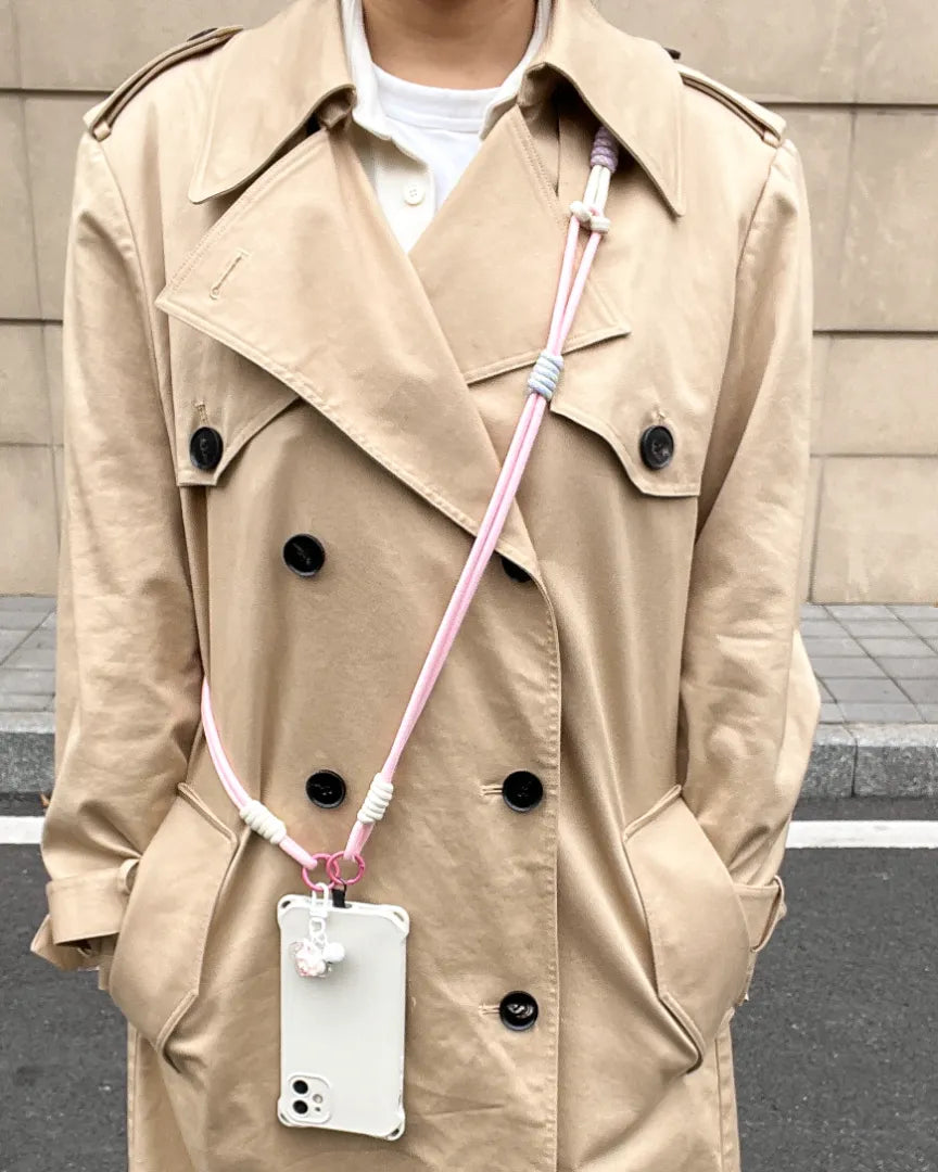 Pink phone strap styled with trench coat outfit, combining feminine color tone with hands free phone carrying#color_pink